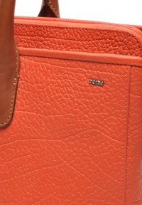 Oranje gewaxt leer tote bag met een bruine leren handgreep en een ritssluiting, met een klein zilverkleurig logo detail aan de voorkant.