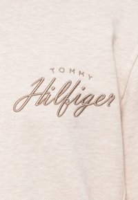 Hosszú ujjú pamut ing világos bézs színben. A mellrészen barna hímzett kurzív betűkkel szerepel a "TOMMY HILFIGER" felirat. Puha, textúrált anyag.