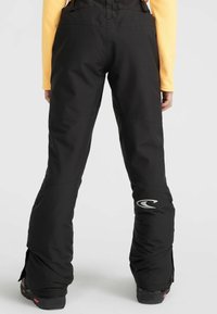 Zwarte sneeuwbroek met versterkte knieën, een lichte glans en een logo op het linkerpoot. Het ontwerp heeft een bootcut met ritsen bij de enkels.