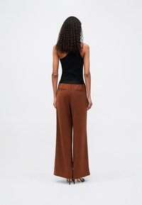 Top negru cu un singur umăr, combinat cu pantaloni largi, cu talie înaltă, de culoare maro, care prezintă buzunare mici la spate și o textură fină.