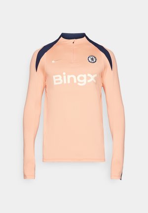 Light pink long-sleeve jersey with navy shoulder accents, high collar, zip closure, and white "Bingx" logo. Features Chelsea FC emblem.