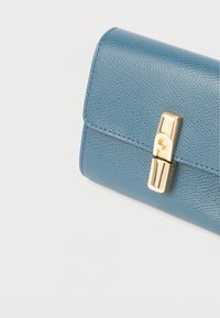 Portofel din piele albastră texturată cu o închizătoare dreptunghiulară aurie pe un fundal alb, prezentat într-un unghi.