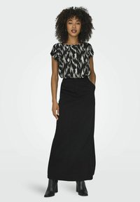 Jupe maxi noire associée à un haut à manches courtes arborant un motif abstrait noir et blanc. Le mannequin porte des bottes à talons noires.