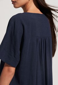 Tumši zils lina kleita ar īsām piedurknēm, ar kroku aizmugures dizainu un apaļu kakla izgriezumu. Gluda tekstūra un brīvs piegriezums.