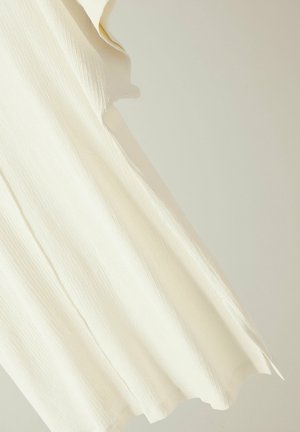 Top color crema con una superficie testurizzata, caratterizzato da un orlo ondulato e un taglio irregolare su una manica per una vestibilità rilassata.