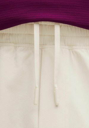 Pantalones con cinturilla elástica color crema y cordones ajustables, combinados con un top de punto morado visible en la cintura.