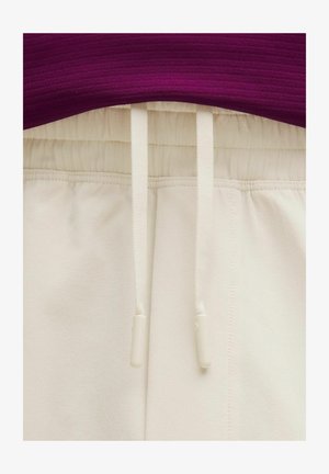 Pantalones con cinturilla elástica color crema y cordones ajustables, combinados con un top de punto morado visible en la cintura.