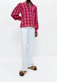 Camicia a maniche lunghe a scacchi rossi e rosa con pattina dei bottoni, abbinata a pantaloni bianchi a gamba larga e sandali con plateau marroni.