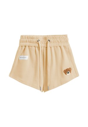 Pantalones cortos beige con cintura elástica y cordón, bolsillos laterales, pequeña etiqueta rectangular a la izquierda y parche con cara de oso de peluche en la pierna derecha.