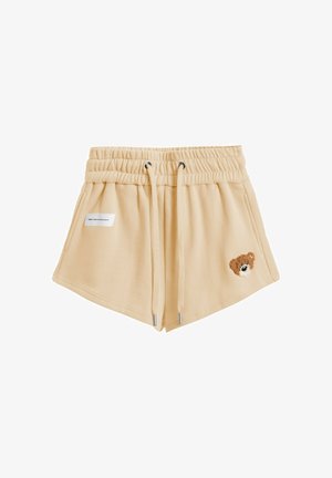 Pantalones cortos beige con cintura elástica y cordón, bolsillos laterales, pequeña etiqueta rectangular a la izquierda y parche con cara de oso de peluche en la pierna derecha.