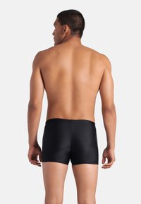 Pantaloni da nuoto neri realizzati in un tessuto morbido e elasticizzato, caratterizzati da un design semplice con una cintura piatta e senza marchi o motivi visibili.