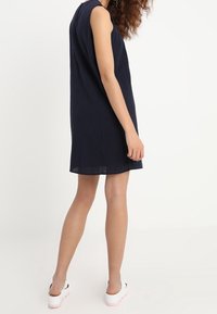 Vestido azul marino de manga corta, corte relajado, tejido texturizado, que llega por encima de la rodilla, combinado con zapatos de plataforma blancos. Diseño minimalista.