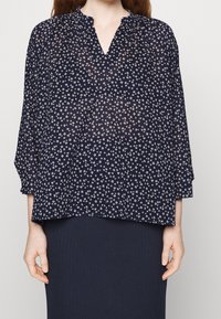 Blusa trasparente blu navy con scollatura a V, caratterizzata da una piccola stampa floreale e maniche a tre quarti; tessuto leggero con una vestibilità ampia.