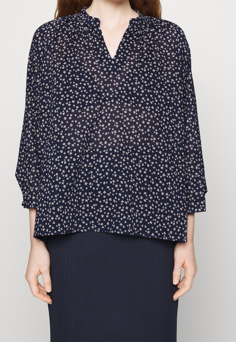 Blusa trasparente blu navy con scollatura a V, caratterizzata da una piccola stampa floreale e maniche a tre quarti; tessuto leggero con una vestibilità ampia.