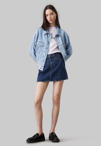 Lichtblauwe denimjasje gedragen over een witte T-shirt met een grafische print. Gecombineerd met een donkerblauwe denimrok en glanzende zwarte schoenen.