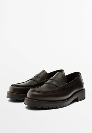 Pair of dark brown leather loafers with thick rubber soles and moc toe stitching on a white background.