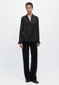 Long black satin button-up shirt with a collar, worn with black velvet wide-leg pants. Simple design, smooth texture, and classic fit.