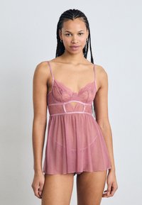 Conjunto de lencería de encaje en suave rosa, que presenta un corsé transparente con detalles recortados, tirantes finos y una falda acampanada con lunares.