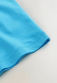 Helles blaues Baumwollgewebe mit einer glatten Textur, das einen abgerundeten Saum und saubere Nähte entlang der Kanten aufweist.