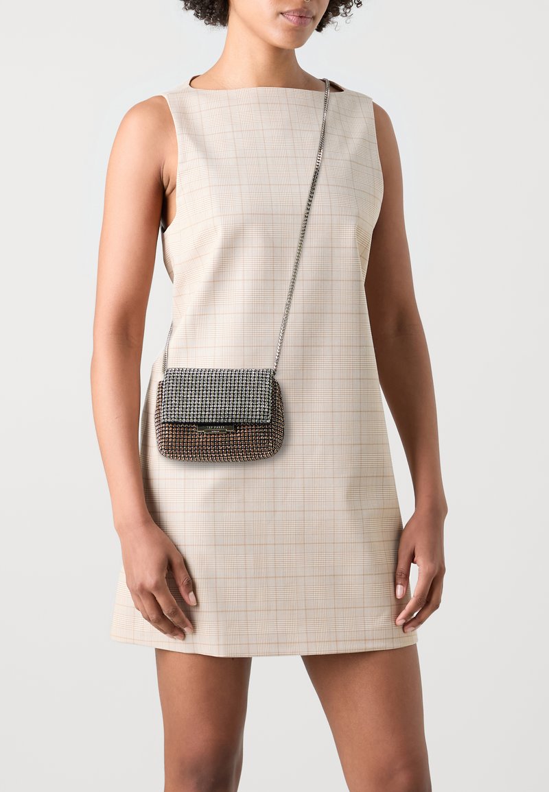 Sølv kæde crossbody taske med metallisk rhinsten dekoration, rektangulær form og klaplukning. Båret over en lys ternet kjole.