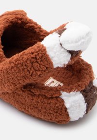 Μαλακά καφέ παιδικά παντοφλάκια με λευκές και σκούρες καφέ λεπτομέρειες, βελούδινη υφή και χαριτωμένη λεπτομέρεια ουράς ζώου στη φτέρνα.