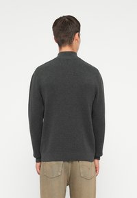 Maglione grigio scuro con colletto alto e polsini a costine, realizzato in un morbido tessuto testurizzato, abbinato a pantaloni beige chiaro.