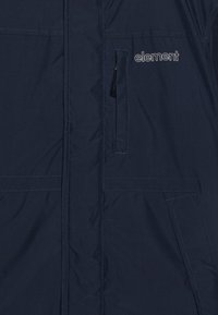 Navy blue jacket featuring a smooth, water-resistant fabric, zippered pocket, and logo detail on the chest. Visible stitching lines.