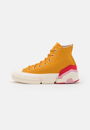 Basket montante jaune moutarde avec lacets blancs, semelle blanche épaisse, et accents rouges et roses au talon.