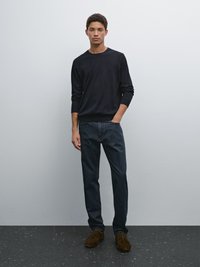 Marinblå crewneck-tröja, mörka denimjeans, bruna mockaskor. Tröjan har lång ärm; jeansen är rakskurna med en blekt textur.