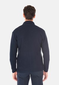 Cardigan lavorato a maglia di colore blu navy con colletto alto, maniche lunghe e tessuto testurizzato. Presenta una cucitura centrale sul retro e polsini a costine.