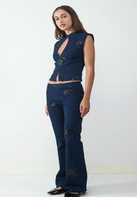 Marineblaue Denim-Zwillingskombination mit einem figurbetonten, ärmellosen Oberteil mit Ausschnitt und schmalen Hosen mit schwarzen, blumigen Paillettenverzierungen.