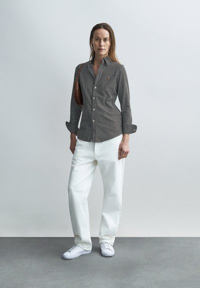 Fekete-fehér csíkos, gombos ing felhajtott ujjakkal, fehér, bő szárú nadrággal és fehér tornacipővel párosítva. Barna válltáska dísz.