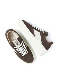 Braune Wildledersneaker mit weißen Akzenten, ausgestattet mit einer dicken weißen Sohle und Schnürdesign. Auffälliges Branding an der Seite und Zunge.