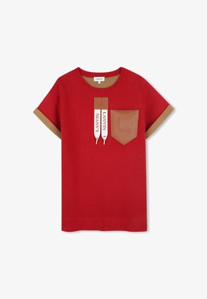 T-shirt en coton rouge à manches courtes, avec des bordures marron, une poche en cuir et des bretelles de marque. Présente un logo bien visible sur la poche.