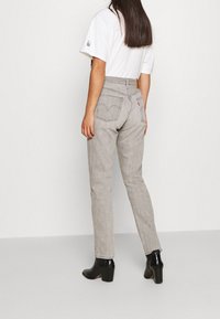 Jeans in denim grigio con vita alta, dotati di tasche posteriori con dettagli cuciti. Abbinati a stivaletti neri con tacco. T-shirt bianca semplice.