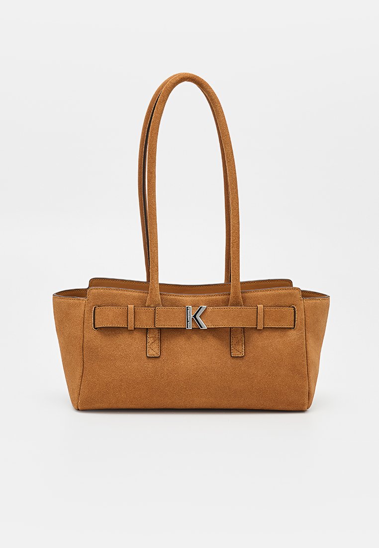 Bolso rectangular de ante marrón con asas dobles largas y tira decorativa con un cierre plateado en forma de "K" sobre un fondo liso.