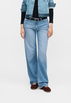 Γυναίκα που φοράει ανοιχτό μπλε τζιν ψηλόμεσο με φαρδιά μπατζάκια, κοντό τζιν μπουφάν, μαύρο μακρυμάνικο τοπ, μαύρη ζώνη και καφέ δερμάτινα παπούτσια με κορδόνια.