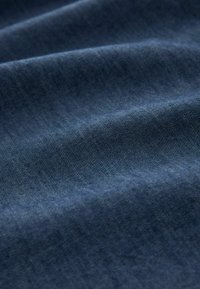 Tissu en denim bleu foncé avec une surface légèrement texturée, présentant des variations subtiles de couleur et une finition lisse et douce.