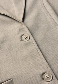 Blazer texturizado beige con cuello con muesca, dos botones con la marca "StreetOne" y un sutil patrón tejido.