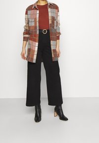 Rutig flanellskjorta i orange, brunt och grått, med två bröstfickor. Kombinerad med högmidjade svarta vida byxor och svarta klackstövlar.