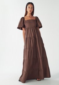 Brown tiered maxi dress with puff sleeves and square neckline, made of soft fabric with gathered details at the bust and waist.