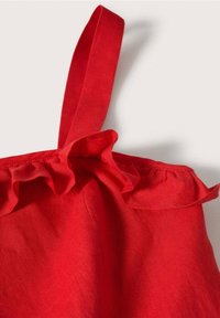 Haut en lin rouge avec bordure à volants et fines bretelles ; le tissu semble lisse avec une finition légèrement texturée près des volants.