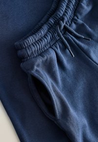 Tumesinised puuvillased joggerpüksid, millel on elastne vöökoht nööriga, küljetaskud ning sile ja pehme tekstuur.