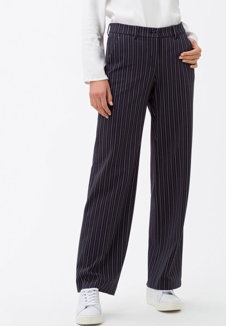 Pantalons rayés bleu marine avec une coupe droite, doté d'une fermeture à bouton et de poches latérales, associés à des baskets blanches.