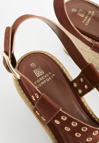 Sandali con tacco in suede marrone, dotati di dettagli in metallo dorato, insole testurizzata e occhielli decorativi sulle cinghie. Suola leggera.