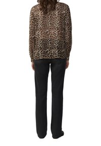Blouse en voile marron à motif léopard, à manches longues et coupe fluide, associée à un pantalon noir à jambes droites.
