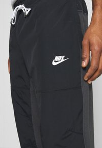 Zwarte sportshorts met grijze zijpanelen, wit Nike-logo op de linker dij en wittekoord zichtbaar boven de tailleband.
