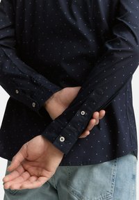 Marineblaues Hemd mit Knöpfen und kleinem hellblauen Rautenmuster, langen Ärmeln und geknöpften Manschetten. Verfügt über eine glatte Textur und eine taillierte Passform.