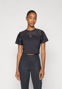 Camiseta atlética negra corta con panel superior texturizado, mangas cortas y un pequeño logo blanco. Combinada con leggings negros de talla alta con patrón.