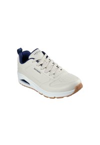 Light beige athletic shoe with navy accents, perforated toe, and thick white sole. Features a padded collar and brown rubber outsole.